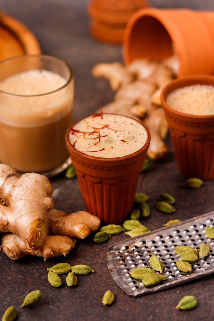 Close-up of masala chai in clay cups surrounded by ginger and cardamom for a rustic look.